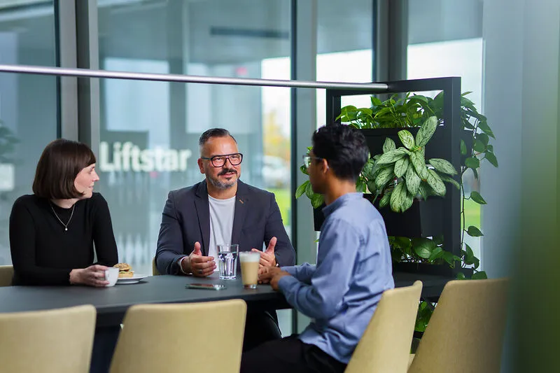 Drei Kollegen bei Liftstar im Gespräch in modernem Büro, freundliche Atmosphäre im Gesundheitsbereich.