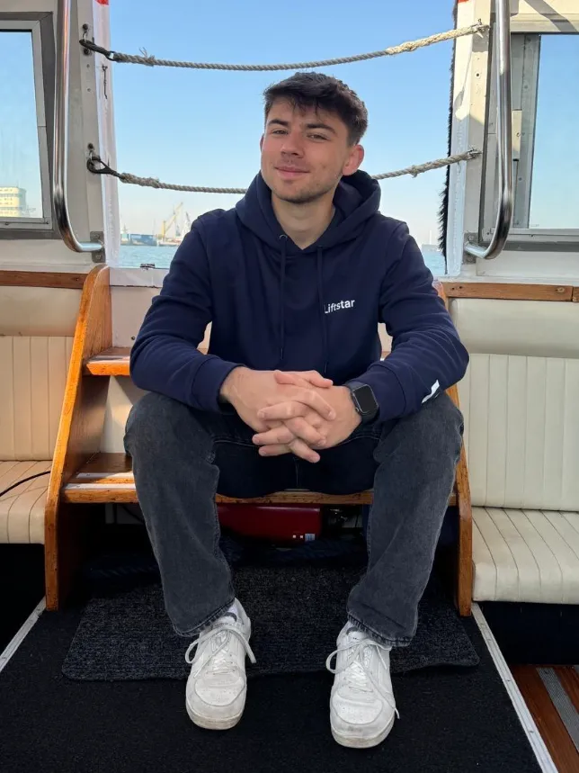 Dualer Student im Liftstar-Hoodie sitzt entspannt auf einer Bootstreppe und lächelt in die Kamera.