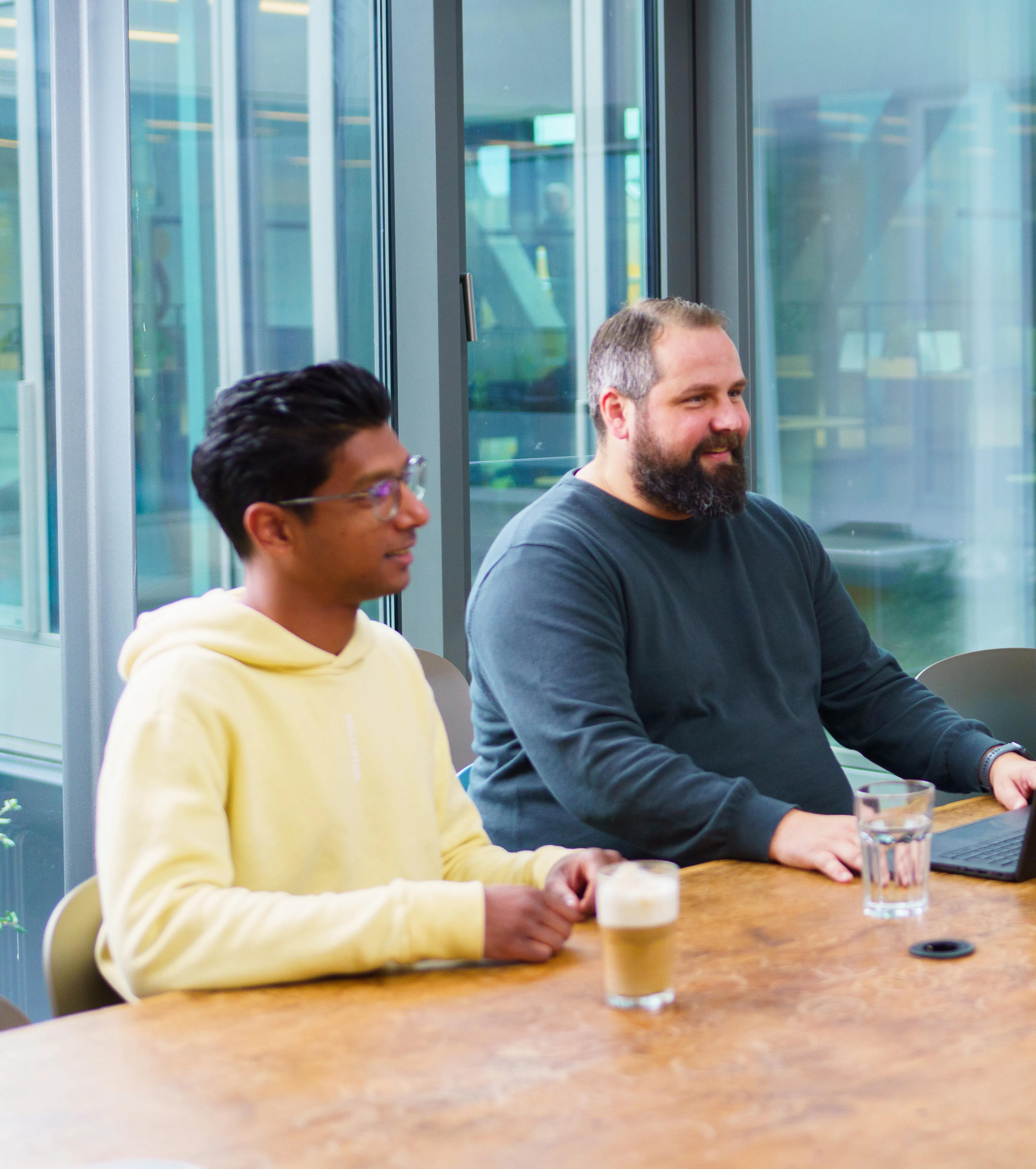 Zwei Kollegen bei Liftstar GmbH sitzen entspannt im modernen Büro und tauschen sich bei Getränken aus.