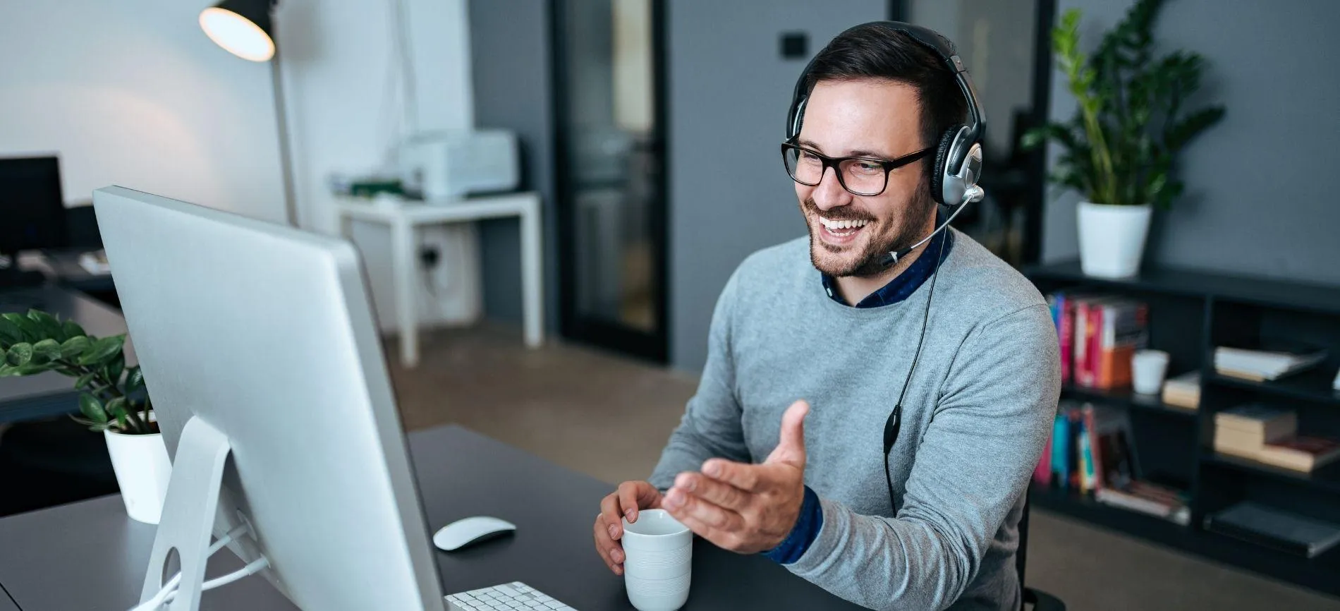 IT-Spezialist mit Headset lacht und spricht mit Dir im Videocall am Schreibtisch bei Logicalis GmbH.