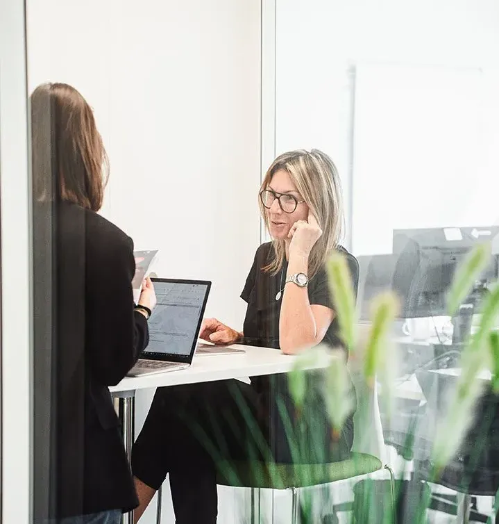 Des collègues discutent dans un salon moderne, un chien à leurs côtés. Ambiance détendue chez Maxi Zoo.