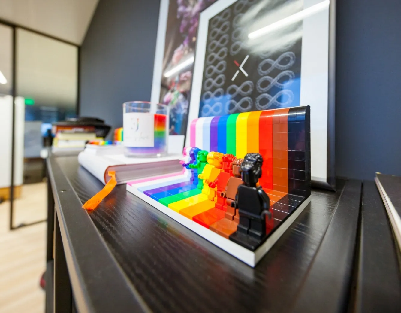 Colorful LEGO figures stand in front of a rainbow wall on a desk, showing off a creative and open office vibe.