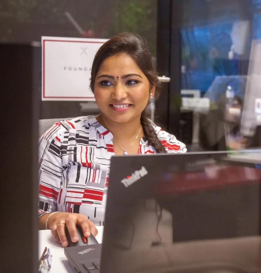 Smiling woman working at her desk with a laptop, giving off friendly, positive vibes in a modern office setting.