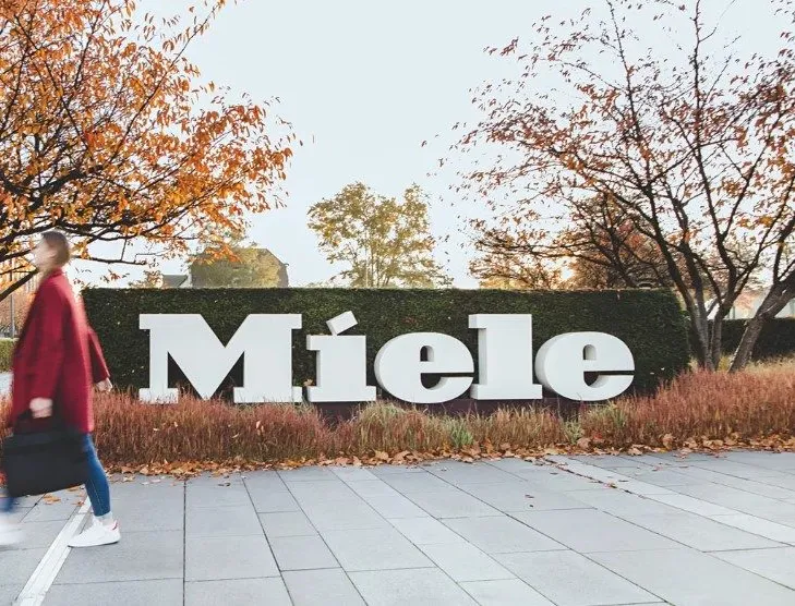 A family stands outside a modern home surrounded by greenery, highlighting Miele's commitment to sustainability.