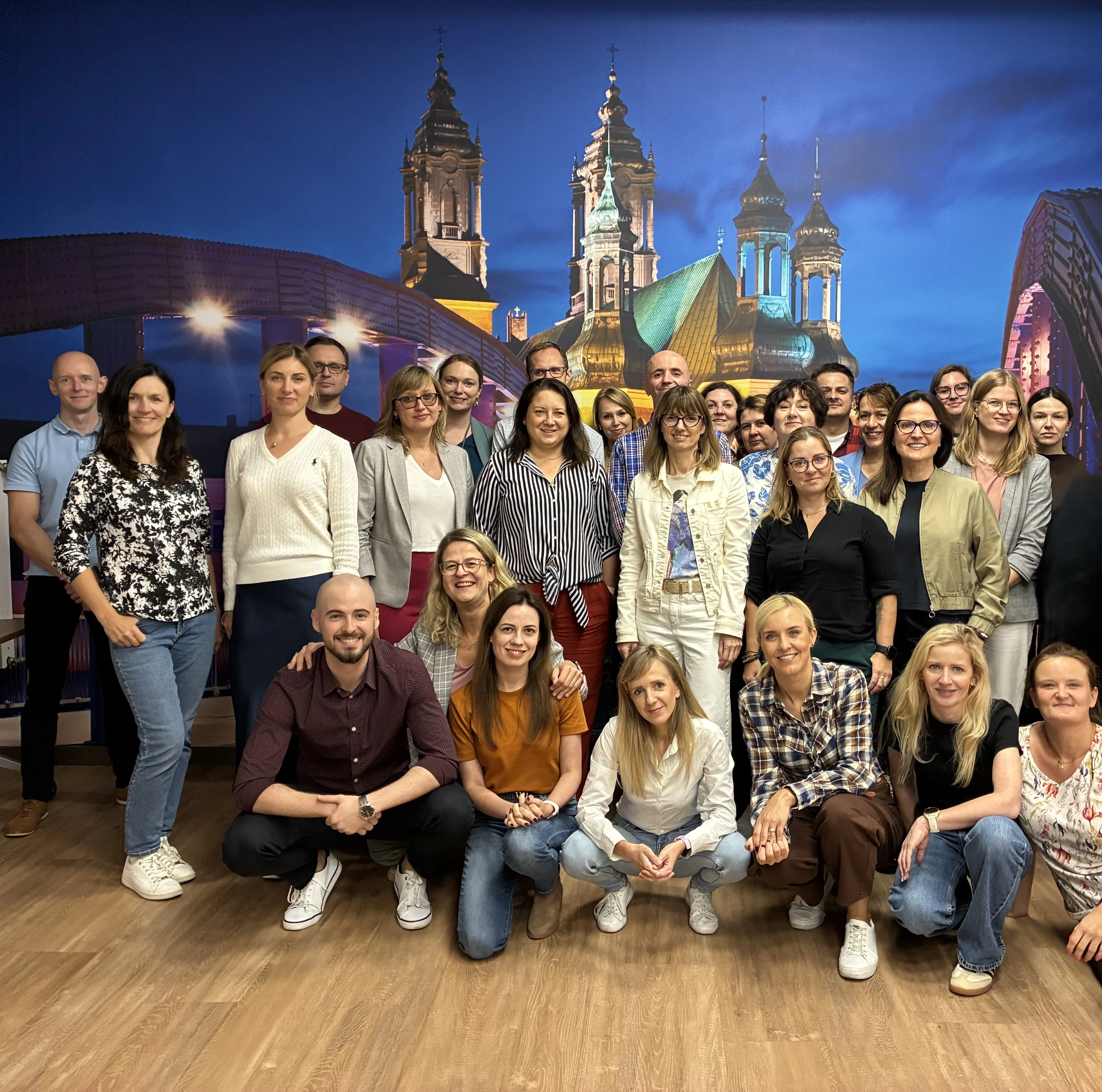 A group of cheerful Miele & Cie. KG employees posing together in front of a vibrant cityscape backdrop, showcasing team spirit.