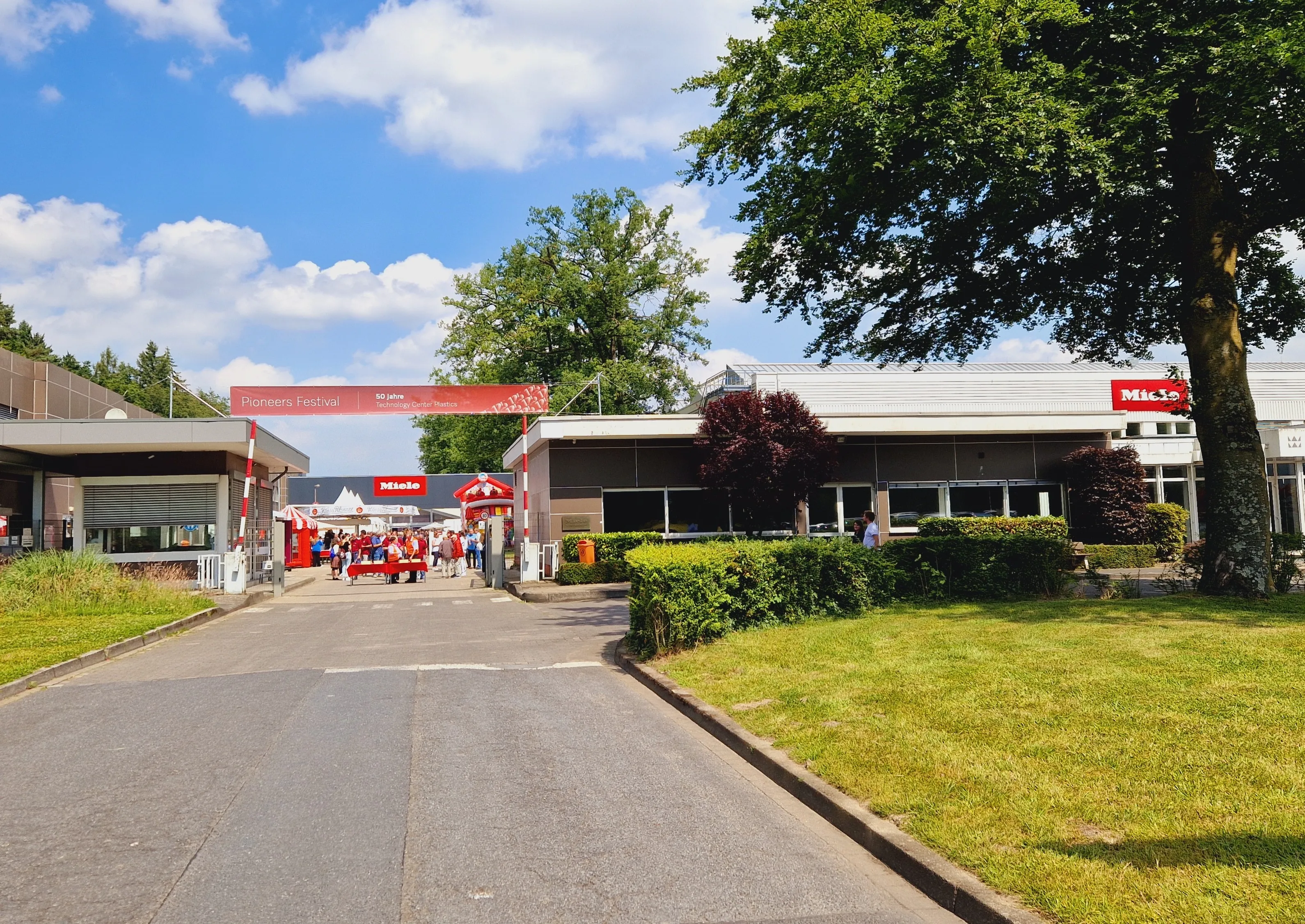 Miele Warendorf: Eingang mit Menschen, die sich in einem sonnigen Industrieumfeld versammeln, um 125 Jahre Miele zu feiern.