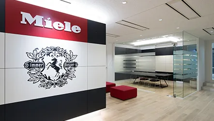 Empfangsbereich bei Miele in Japan mit Logo an der Wand und moderner Sitzgruppe im Hintergrund.