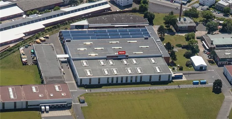 Luftaufnahme des Miele-Werks Euskirchen mit Solaranlagen auf dem Dach, umgeben von Grünflächen und weiteren Gebäuden.