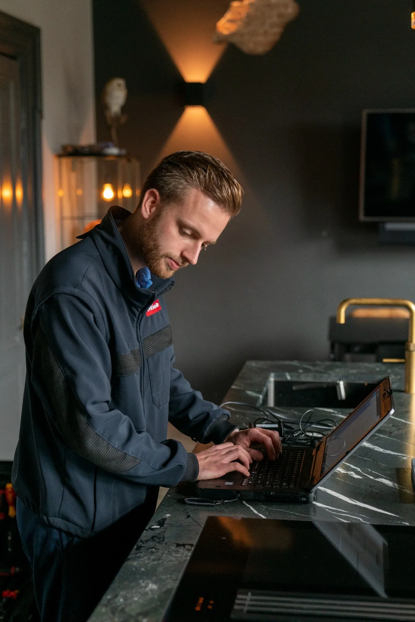 A smiling woman with shoulder-length hair sitting at a desk in a modern office of Miele & Cie. KG, with a laptop and documents in front of her.
