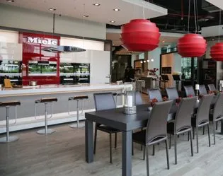 Modern office kitchen at Miele in Turkiye with sleek counters, bar stools, and red pendant lights. Perfect spot for casual chats!