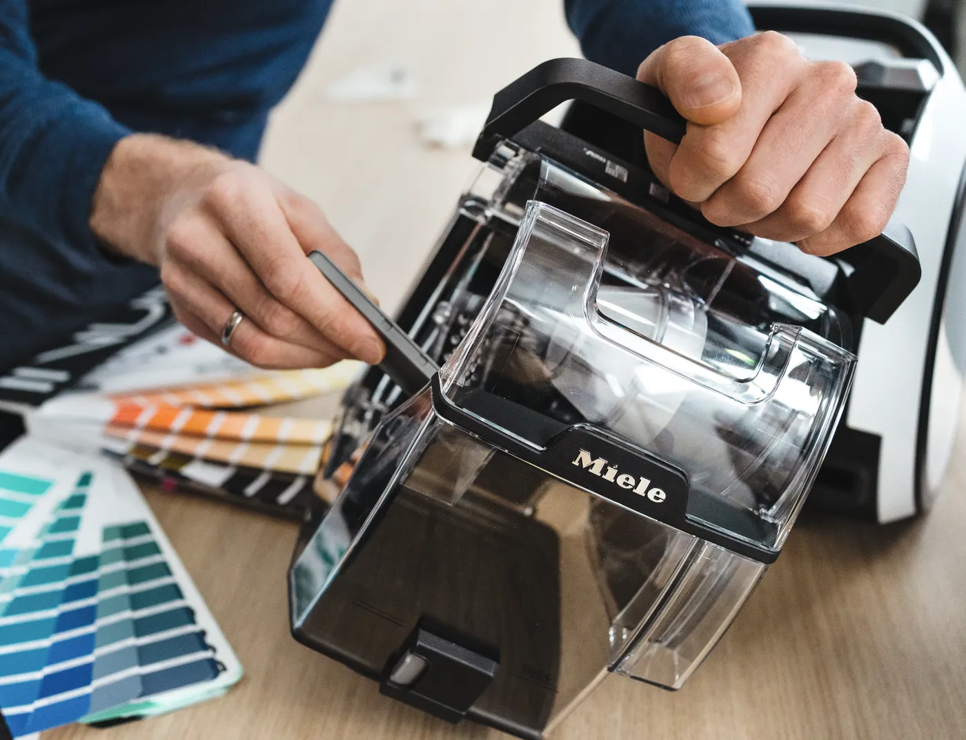 Ein Techniker überprüft einen Staubbehälter von Miele mit Farbmusterfächern im Hintergrund.
