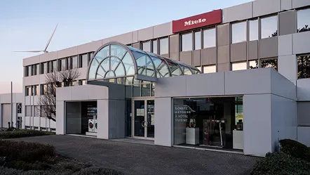 Modern Miele office building in Belgium with a glass entrance, wind turbine visible in the background.