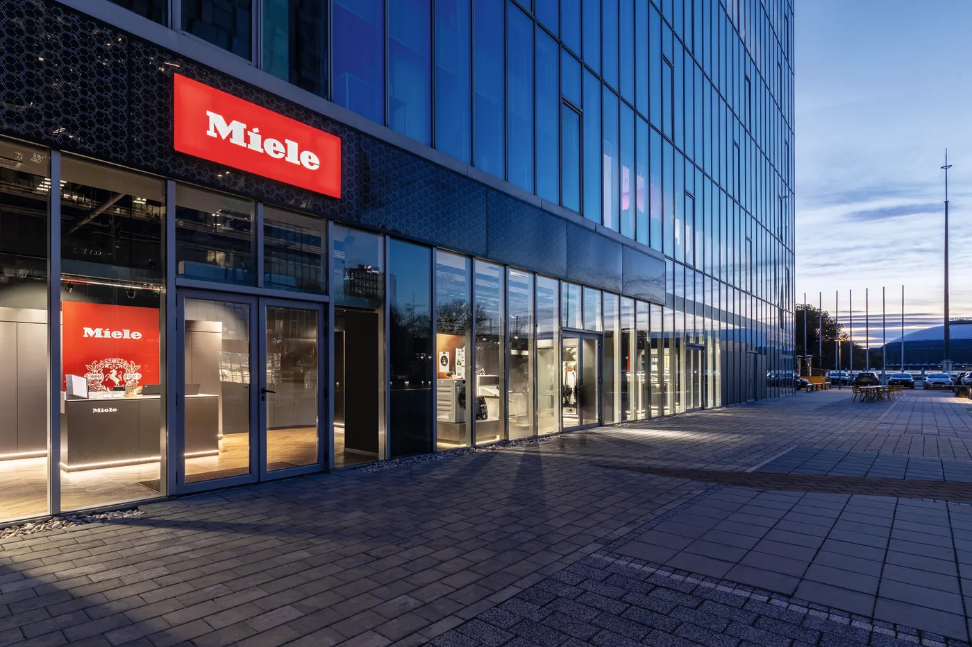 Modern Miele building exterior in Romania at dusk, with sleek glass facade and glowing red signage.