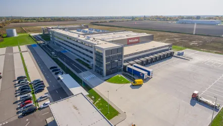 Aerial view of a Miele manufacturing facility in Ksawerov with parking and loading docks, set in a vast landscape.