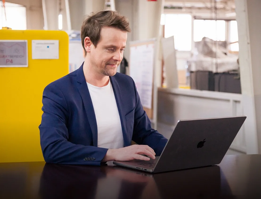 Young woman smiling and working on a laptop in a modern office booth at Miele & Cie. KG, showing a relaxed work vibe.