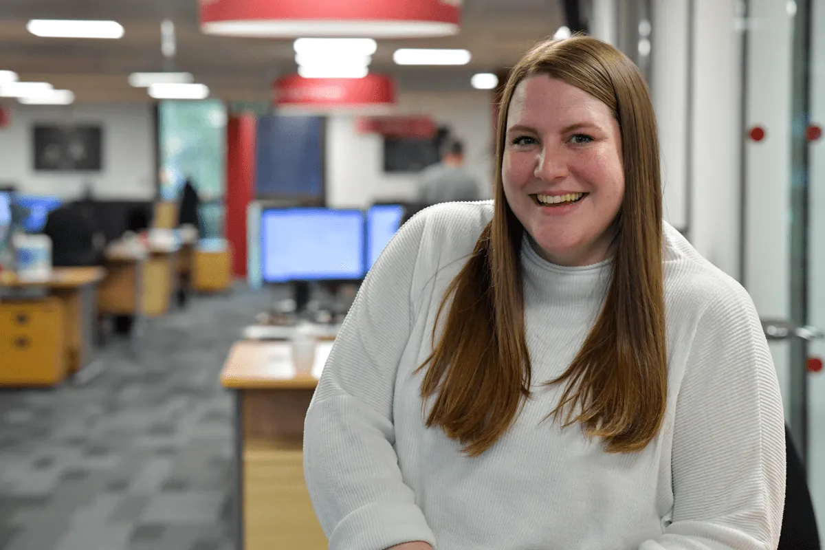 Hannah from HR Operations in a cozy office at Miele & Cie. KG, smiling and ready to help. Join the team in manufacturing!