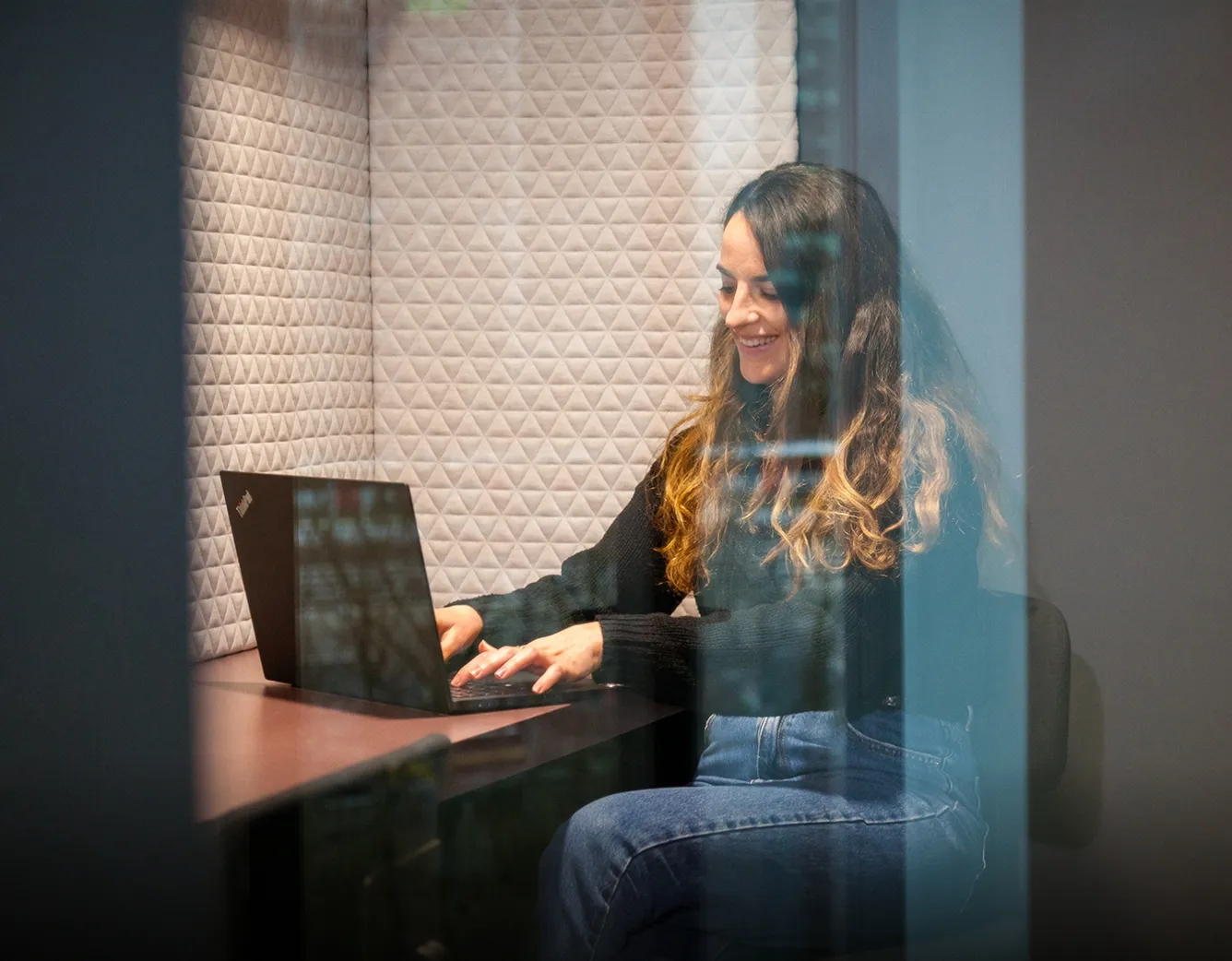 Smiling woman working on a laptop in a cozy office booth, showing a relaxed vibe at Miele & Cie. KG.