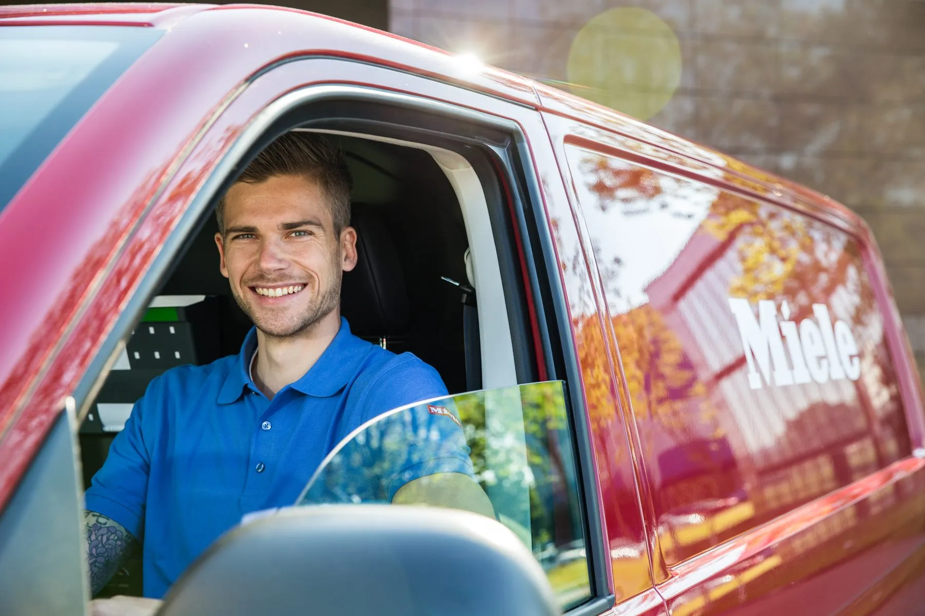 Ein lächelnder Mann in einem Miele-Servicetechniker-Wagen trägt ein blaues Polohemd.