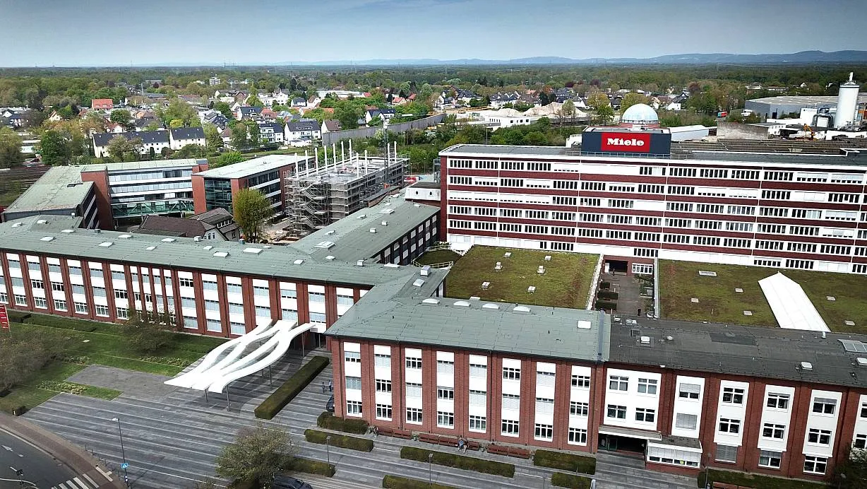 Luftaufnahme des Miele-Werksgeländes Gütersloh mit mehreren roten Backsteingebäuden und grünem Dach.