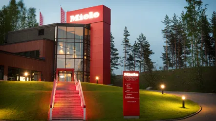 Welcome to Miele Finland: A stunning entrance to our modern facility, nestled amidst lush greenery, ready for your career adventure!