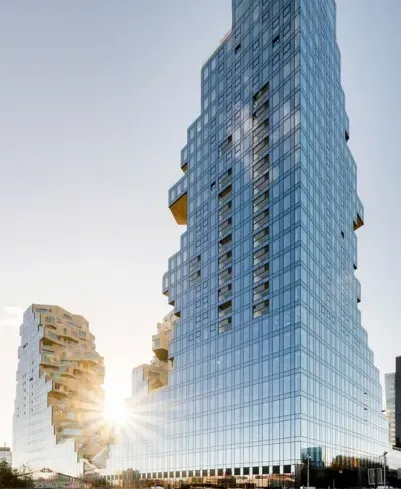 Modern kantoorgebouw van Miele X met een opvallende glazen gevel en terrassen in verschillende niveaus. Het zonlicht schijnt tussen de gebouwen door, wat een heldere en uitnodigende sfeer creëert.