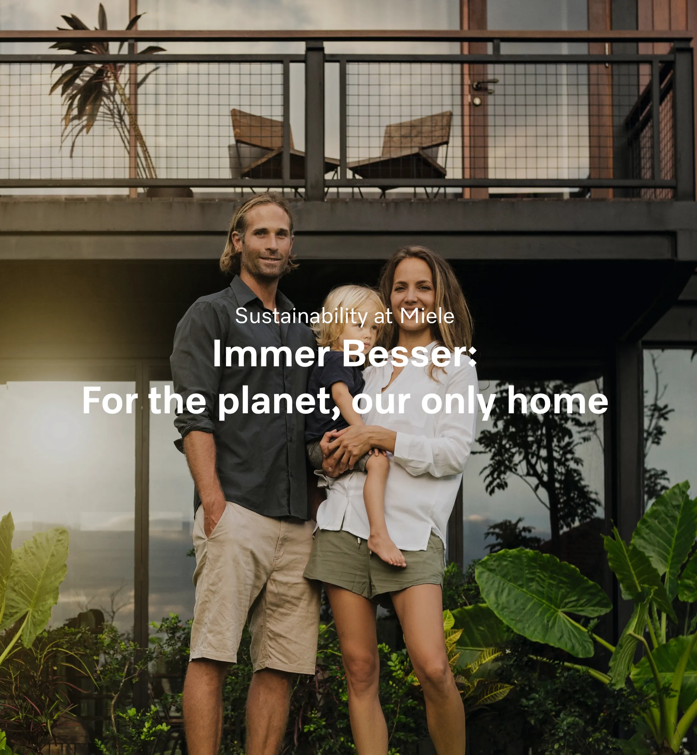 A smiling family stands in front of a modern home surrounded by plants, highlighting Miele’s focus on sustainability.