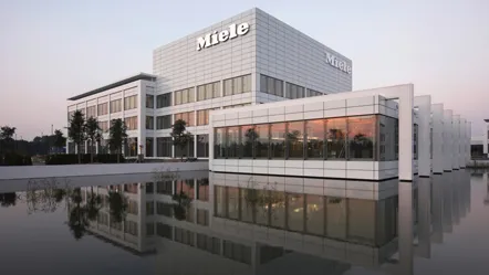 Het moderne hoofdkantoor van Miele Nederlande weerspiegelt in het water bij zonsondergang.