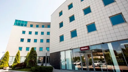A modern Miele office building in Croatia with a glass façade and entrance area, surrounded by well-maintained green spaces