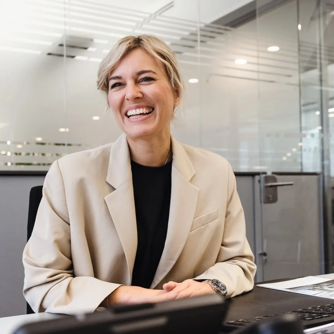 Eine lächelnde Frau in einem Büro bei Miele & Cie. KG, die vor einem Laptop sitzt.