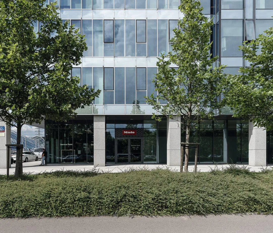 Modern Miele office building in Poland with glass facade and greenery, perfect for aspiring manufacturing professionals.