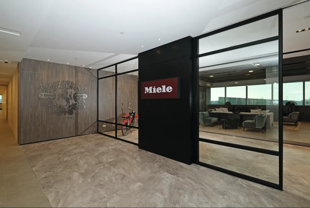 Flur im Miele-Büro in Singapur mit modernem Empfangsbereich, Miele-Logo an der Wand und einem dekorativen Motorrad.