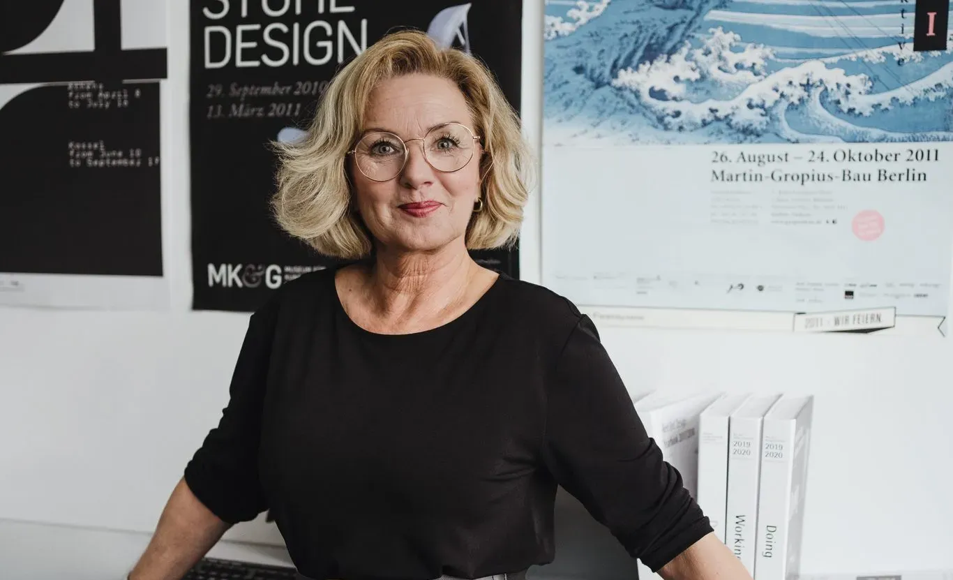 Eine lächelnde Frau in einem schwarzen Oberteil vor einer Wand mit Postern