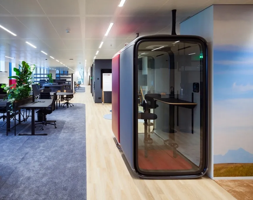 Modern Miele office space with open desks, plants, and a cozy glass meeting pod for focused work or calls.