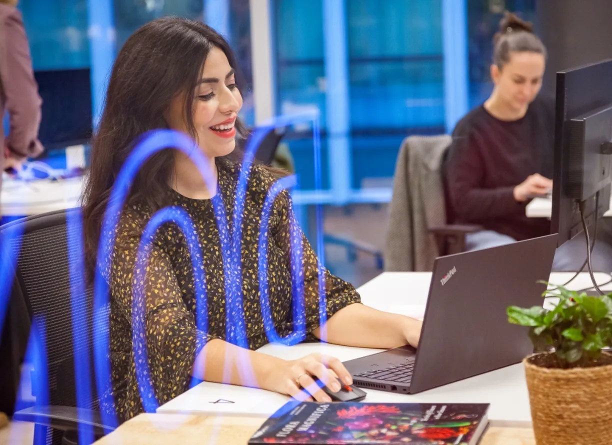 Young woman smiling while working on her laptop at a bright, modern Miele office. Friendly and relaxed vibe.