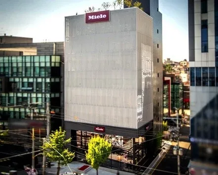 Ein modernes Gebäude von Miele & Cie. KG in Korea in einem städtischen Umfeld, umgeben von weiteren Geschäftsgebäuden.