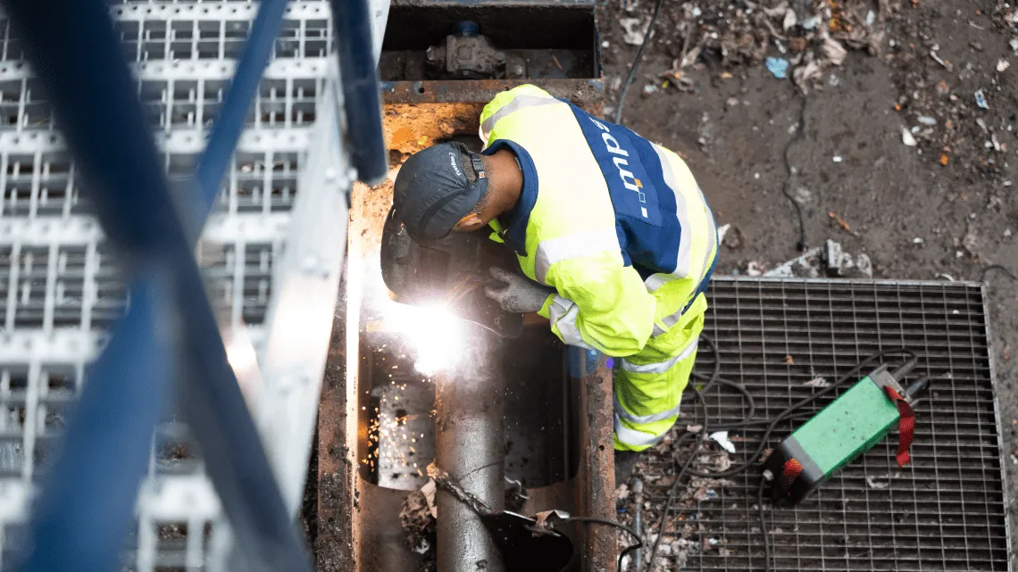 Ein Bauarbeiter mit Schutzkleidung schweißt an einer Metallkonstruktion auf einer Baustelle.