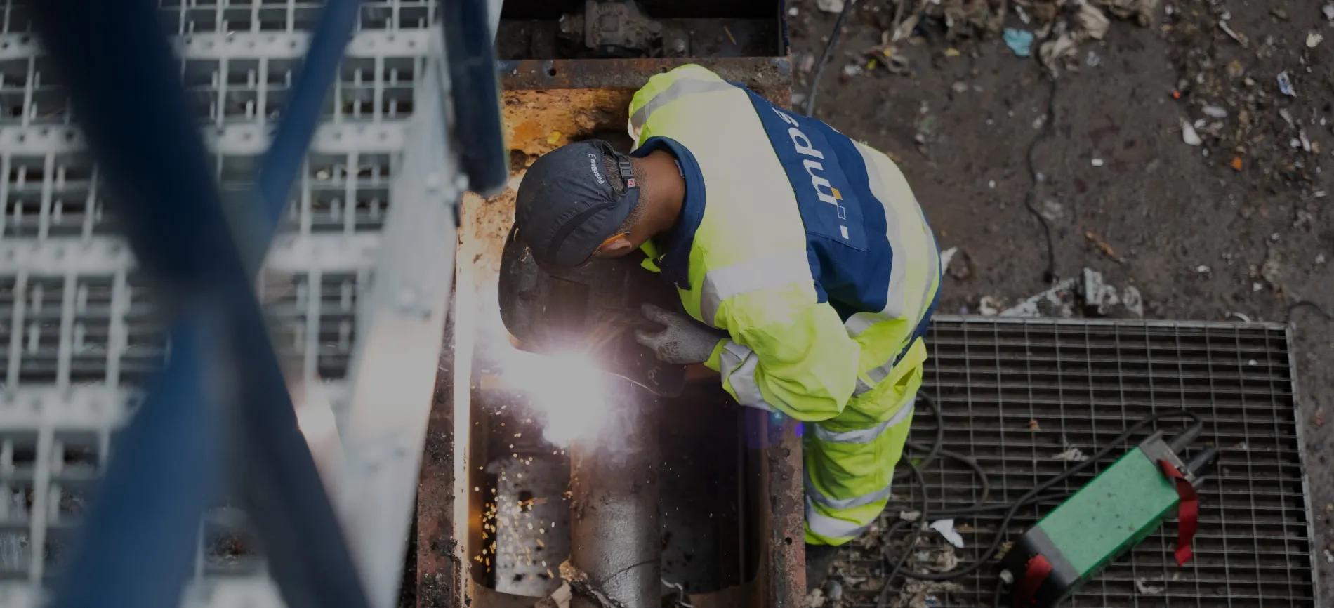 Du siehst einen Bauarbeiter in Schutzkleidung beim Schweißen auf einer industriellen Baustelle von MPS.