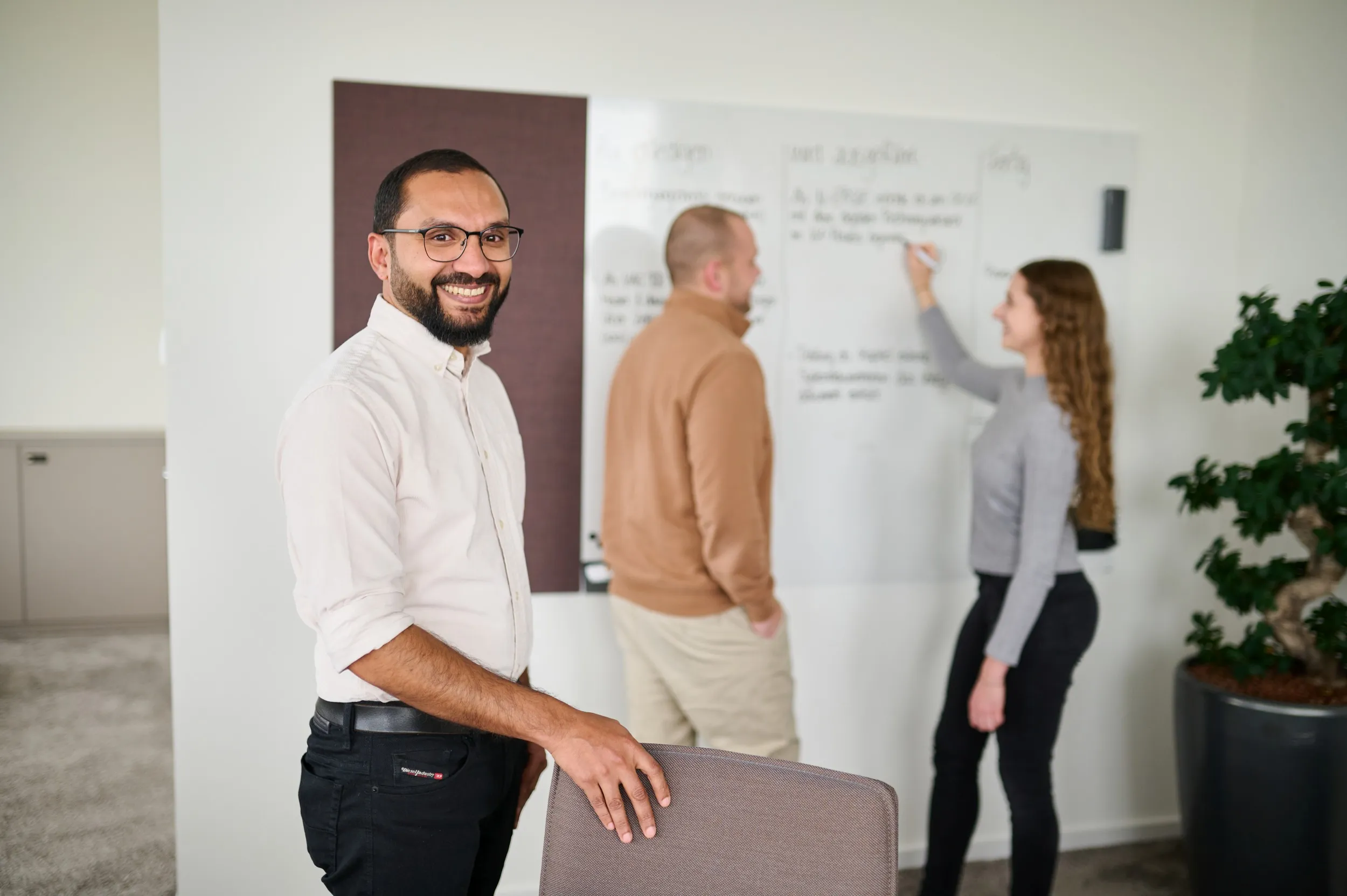 Drei junge Kolleg:innen bei N-ERGIE arbeiten gemeinsam an einer Tafel und tauschen sich im modernen Büro aus.