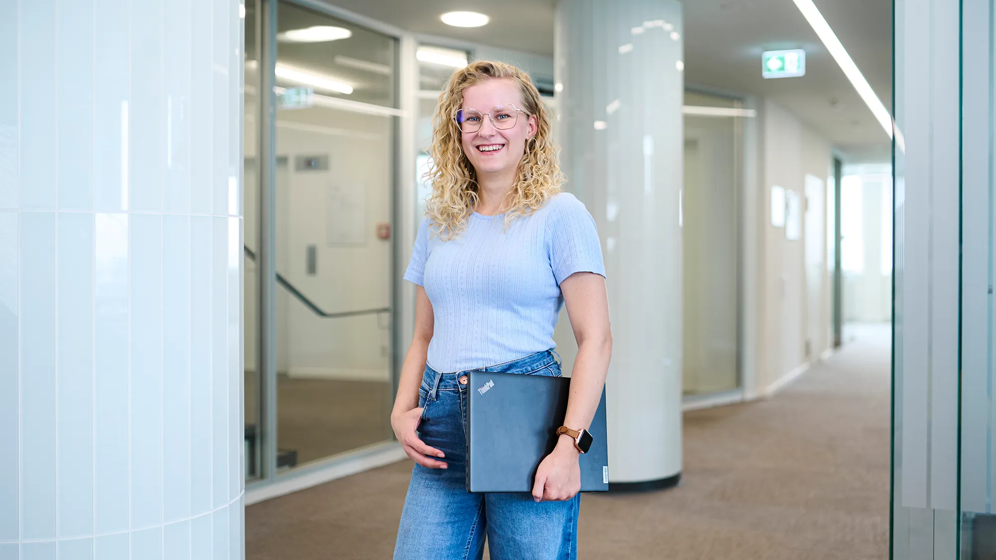 Junge Frau mit Laptop lächelt im modernen Büro von N-ERGIE – starte Deine Karriere in der Energiebranche.