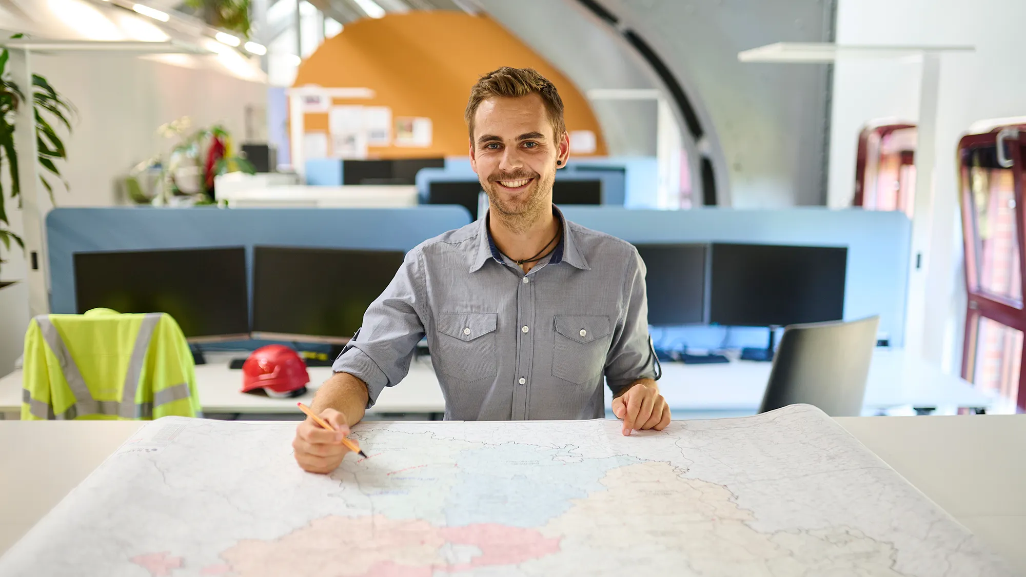 Ein lächelnder Mitarbeiter plant mit einer großen Landkarte im modernen N-ERGIE Büro deinen nächsten Karriereschritt.