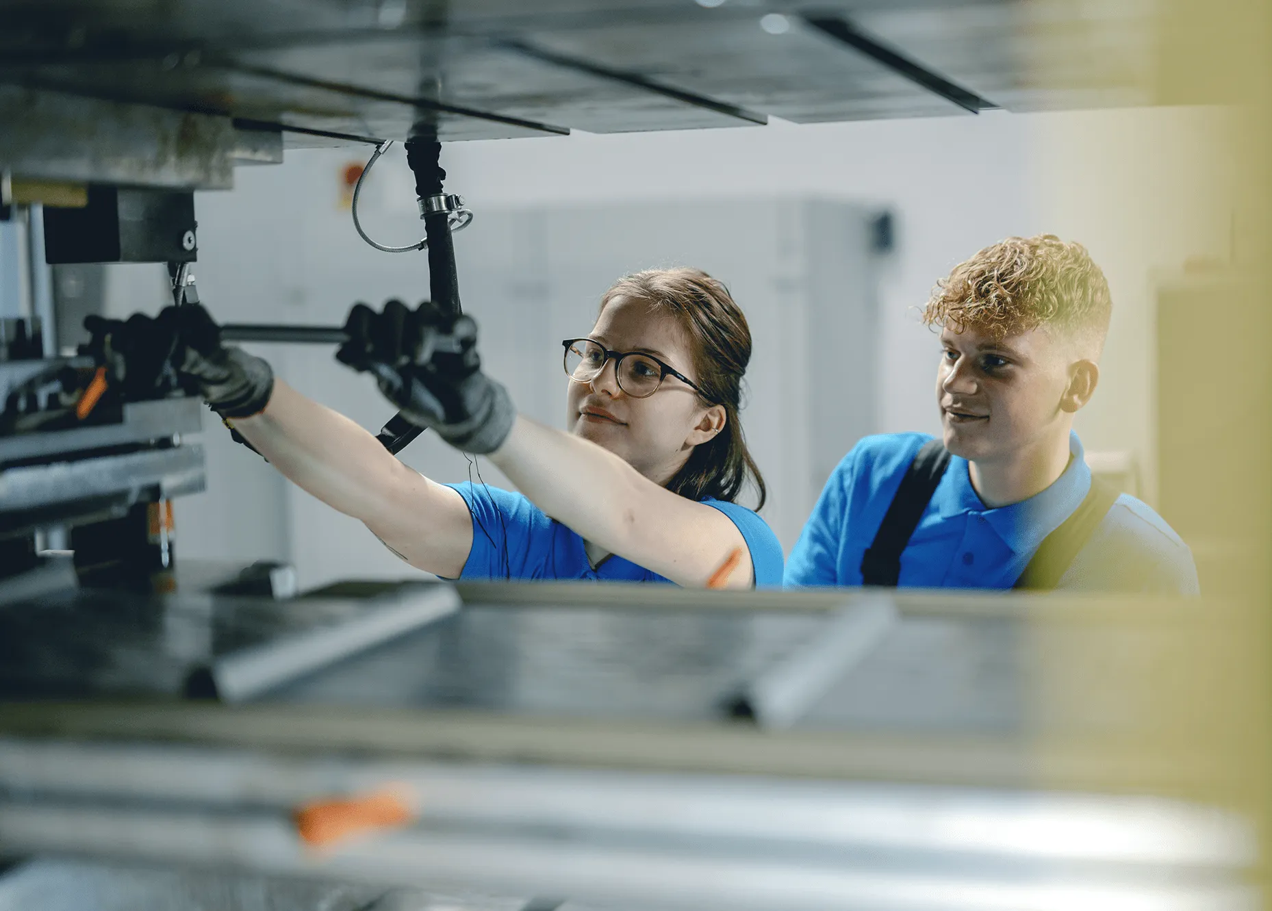 Zwei Personen in blauen Arbeitskleidung bedienen gemeinsam eine Industriemaschine in einer Fabrikumgebung.