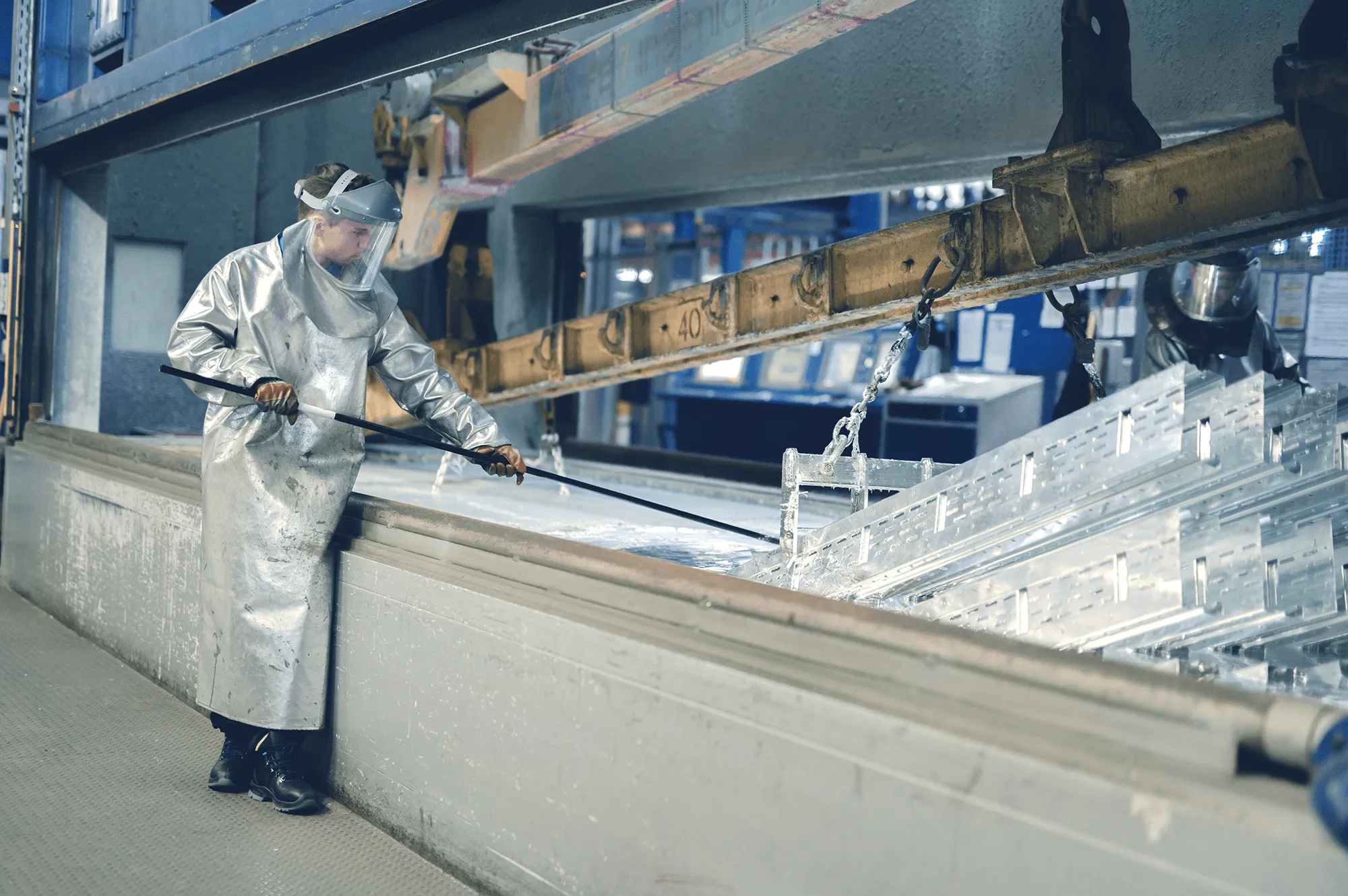 Ein Arbeiter in Schutzkleidung überwacht den Tauchprozess von Metallteilen in einer industriellen Fertigungsanlage.