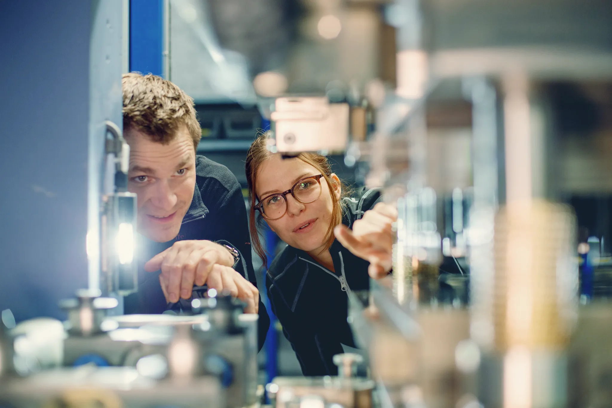 Zwei Fachkräfte inspizieren gemeinsam eine industrielle Maschine in einer Werkhalle.