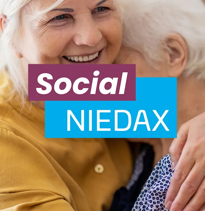 Zwei ältere Personen umarmen sich lächelnd, mit dem Text 'Social Niedax' darüber.