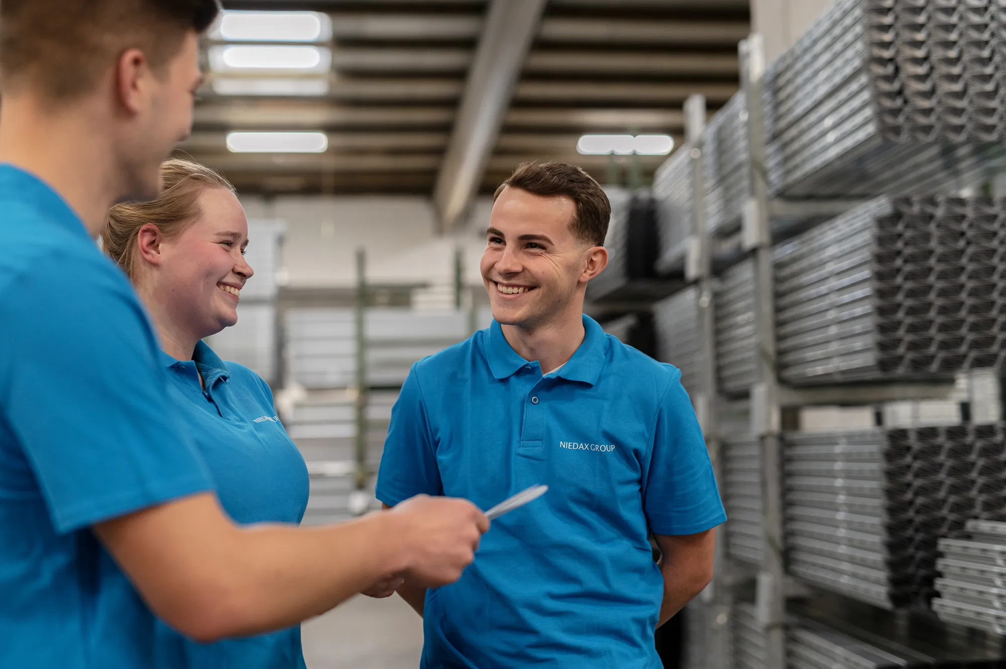 Mitarbeiter der Niedax Group in blauen Polohemden, lächelnd im Gespräch in einer Lagerhalle.