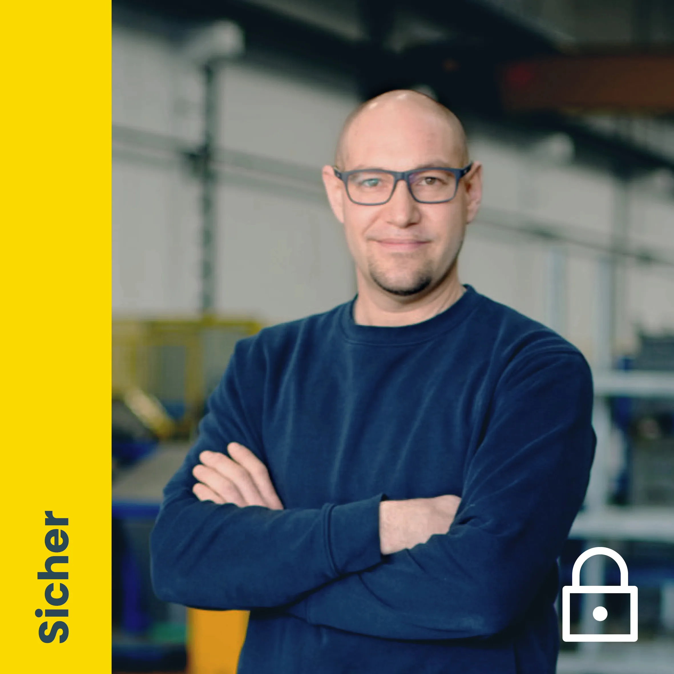 Ein lächelnder Mann mit Brille und verschränkten Armen in einer Produktionshalle, mit dem Wort "Sicher" im gelben Bereich.