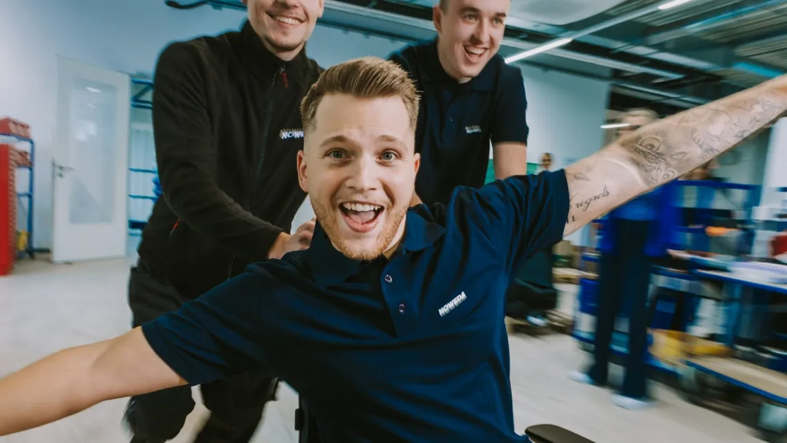 Drei junge Kollegen haben Spaß bei der Arbeit im NOWEDA-Lager, einer lacht fröhlich in die Kamera.