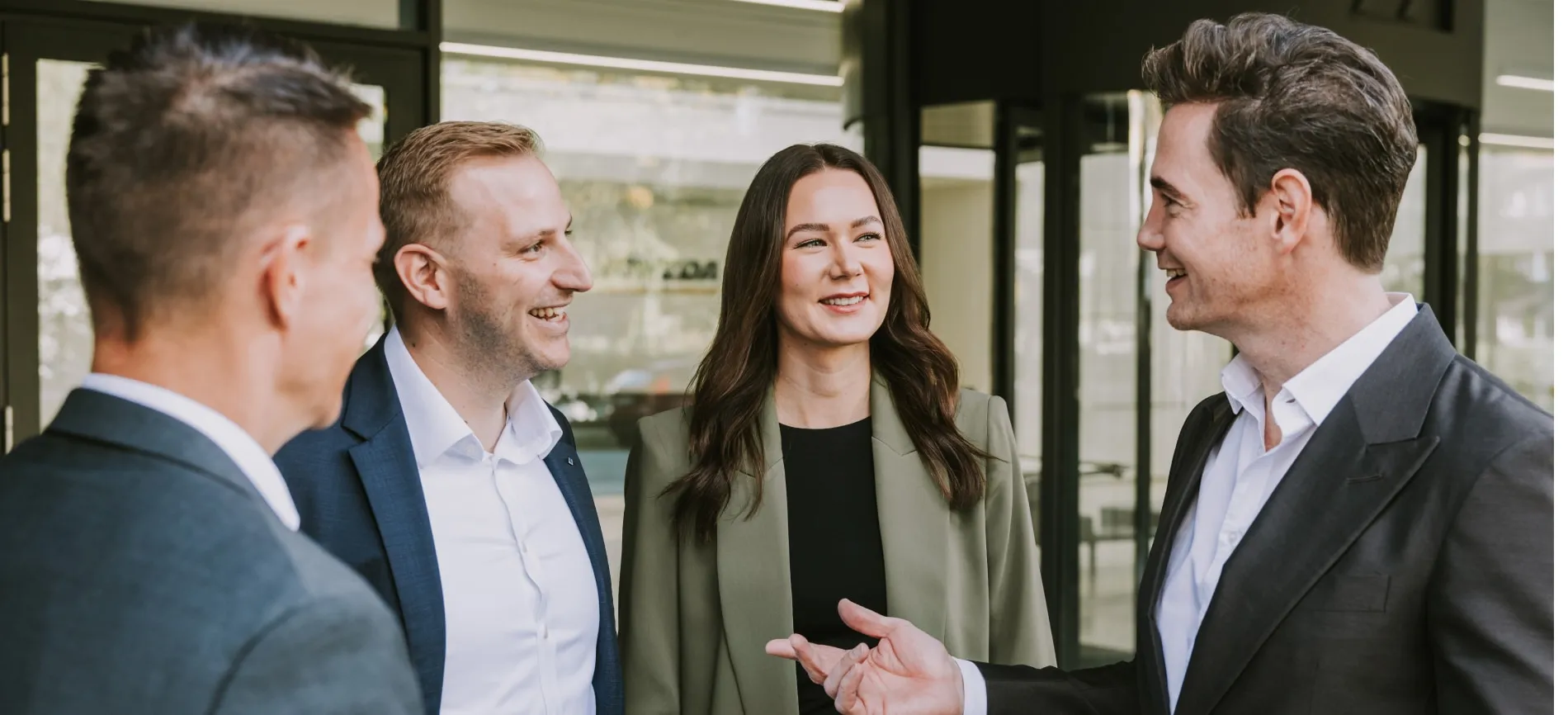 Vier junge Kolleg:innen im Business-Outfit lachen und unterhalten sich vor dem NOWEDA Firmengebäude.
