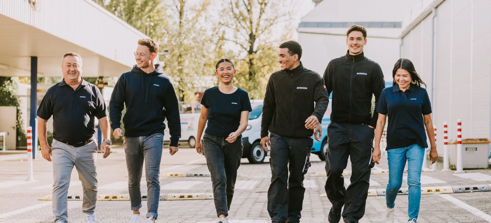 Sechs NOWEDA Mitarbeitende gehen lächelnd gemeinsam draußen, Teamgeist und Freude im Arbeitsalltag stehen im Fokus.