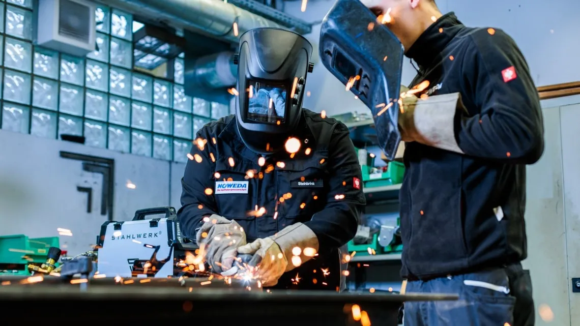 Zwei Personen beim Schweißen in einer Werkstatt von NOWEDA, Funken fliegen. Eine trägt einen Schweißhelm.